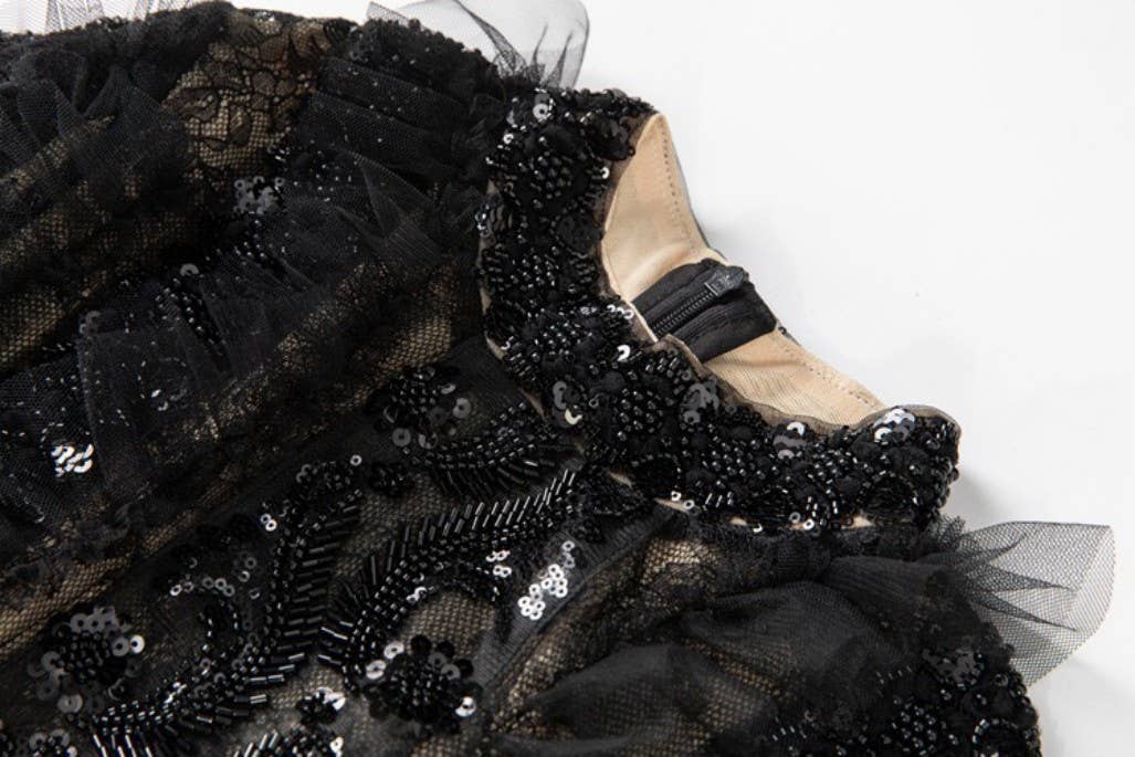 Close up of a black beaded and sequined dress with a white background