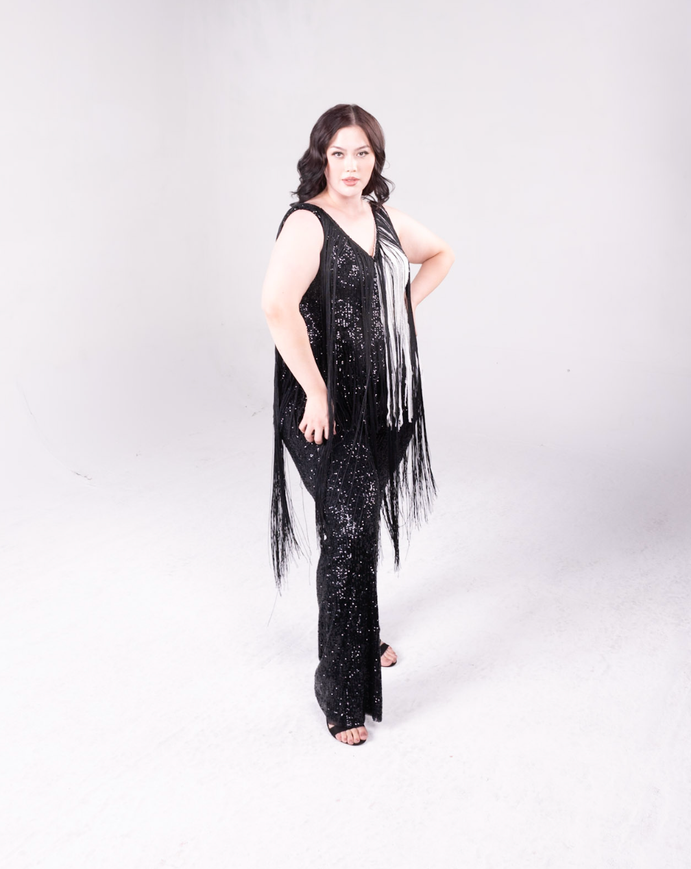sequin fringe jumpsuit with color block detail. One side is all black, and a portion of it is white. Fringe hangs down from the neckline around the bodice of the jumpsuit