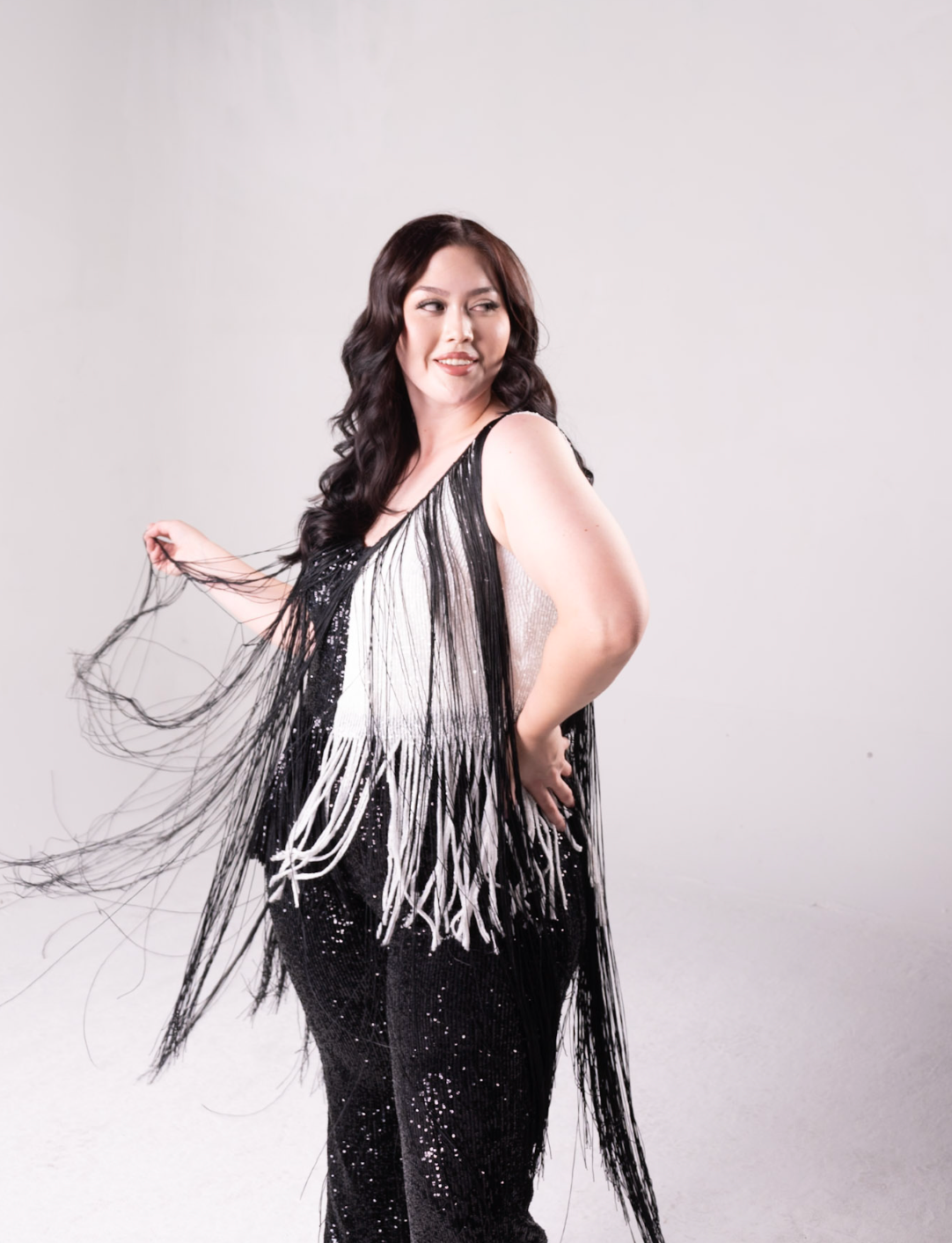 sequin fringe jumpsuit with color block detail. One side is all black, and a portion of it is white. Fringe hangs down from the neckline around the bodice of the jumpsuit
