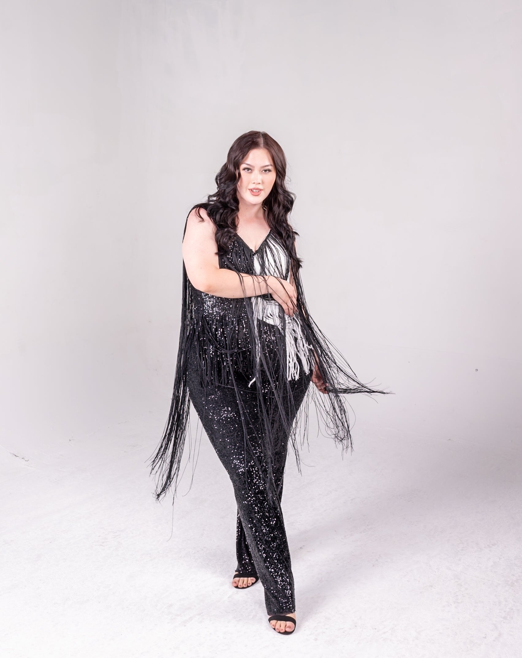 sequin fringe jumpsuit with color block detail. One side is all black, and a portion of it is white. Fringe hangs down from the neckline around the bodice of the jumpsuit