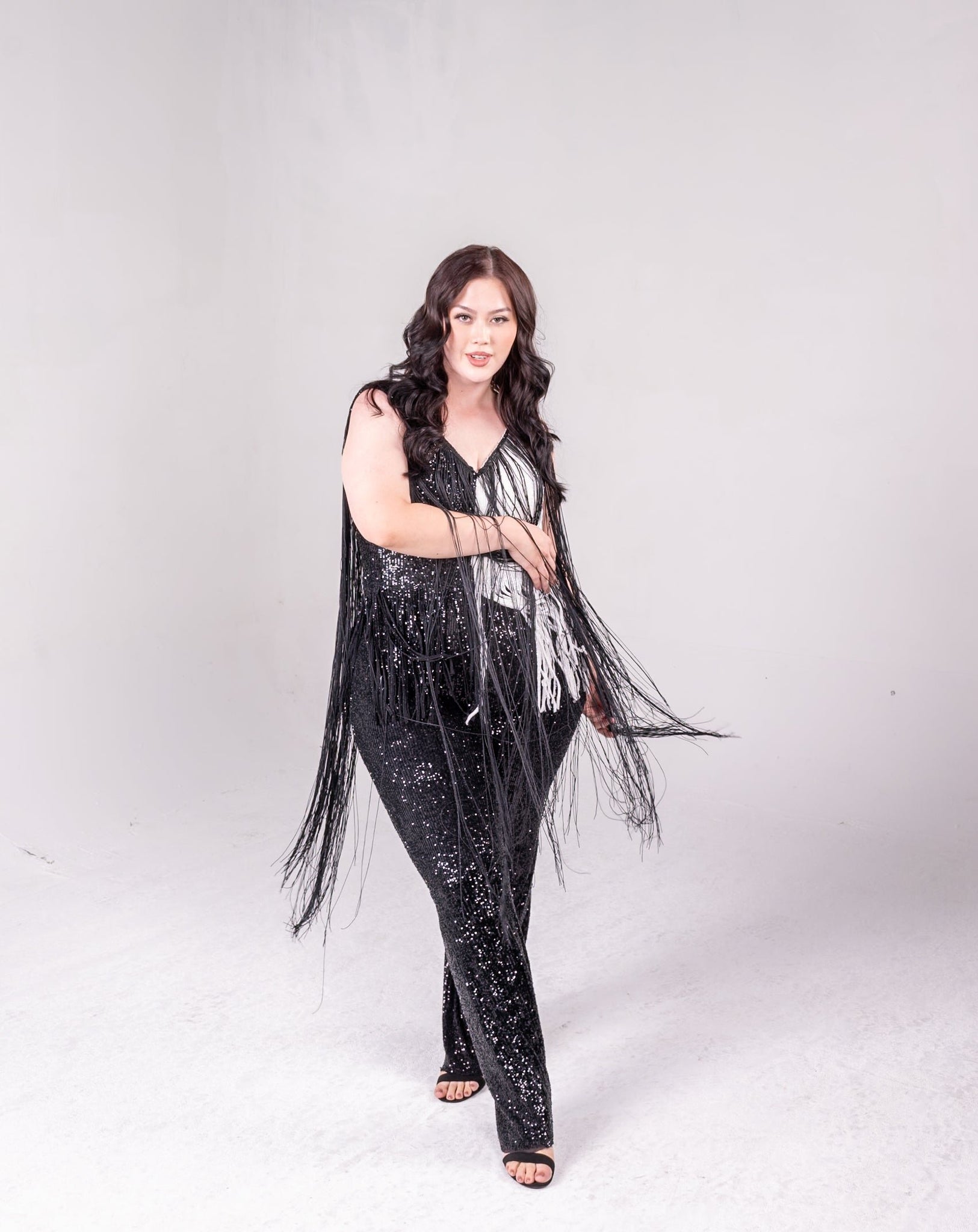 sequin fringe jumpsuit with color block detail. One side is all black, and a portion of it is white. Fringe hangs down from the neckline around the bodice of the jumpsuit