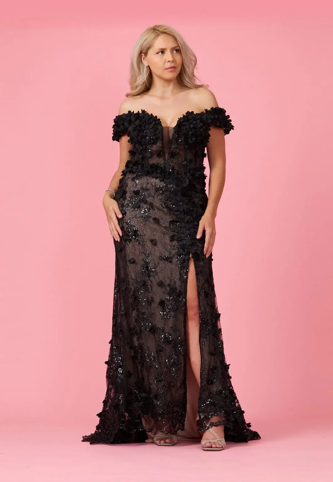 A model wearing an off-the-shoulder, full-length black gown with 3D floral corset detailing and a split on the left side.