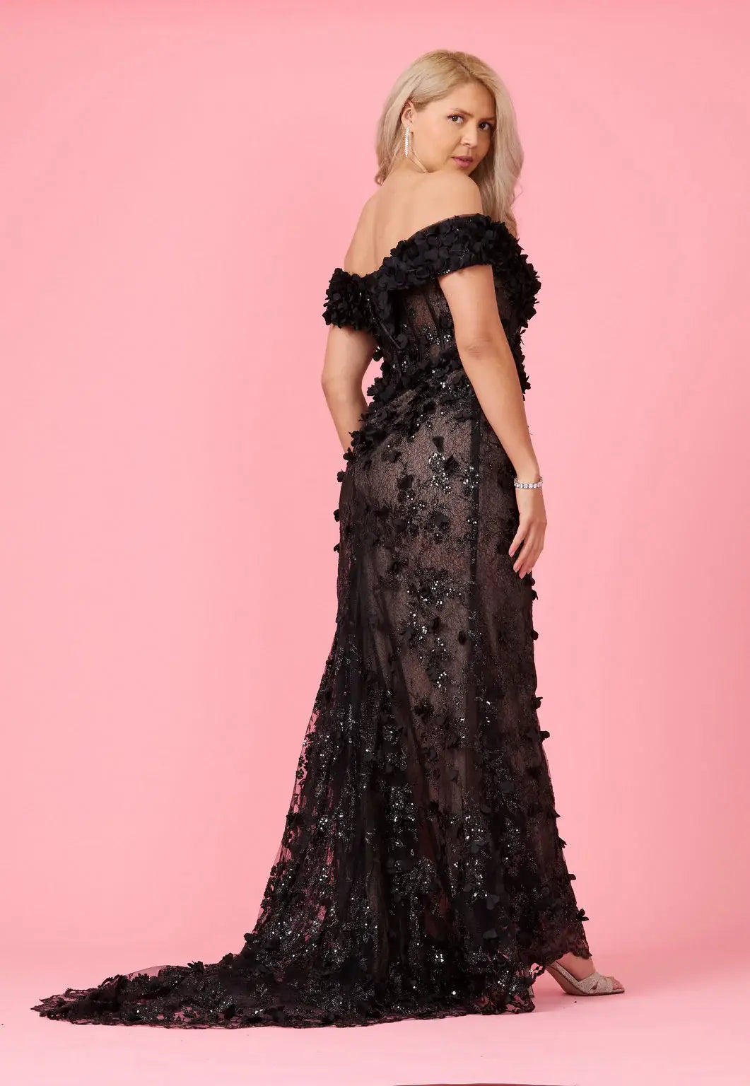 A model wearing an off-the-shoulder, full-length black gown with 3D floral corset detailing and a sweeping train.