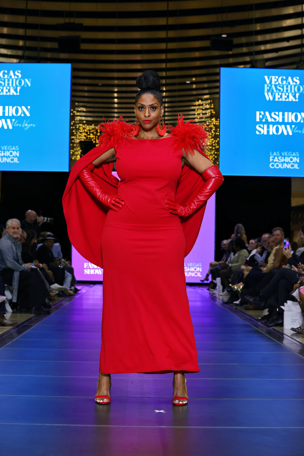 A woman in a red dress with feather details on a runway at a fashion show 