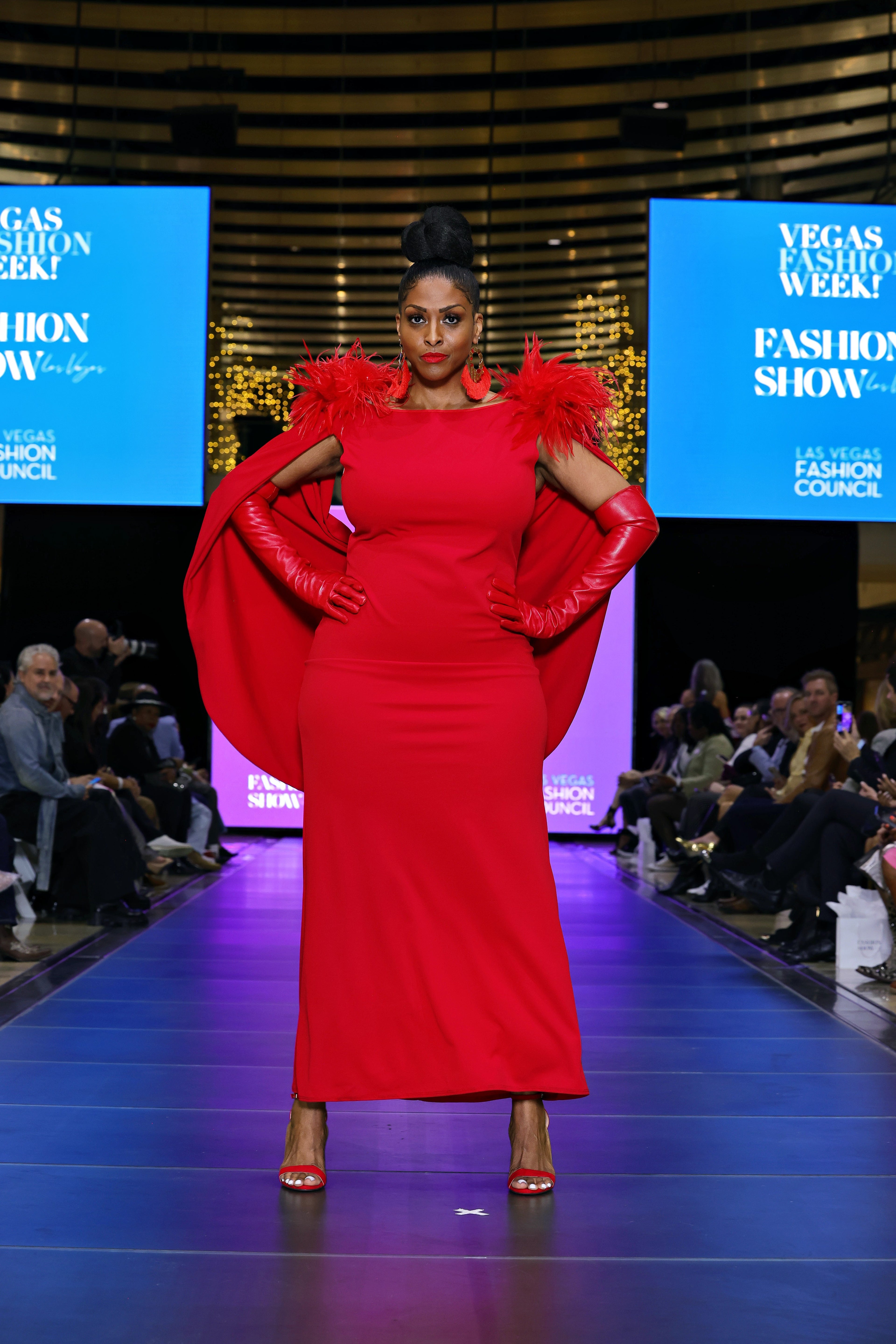 A woman in a red dress with feather details on a runway at a fashion show 