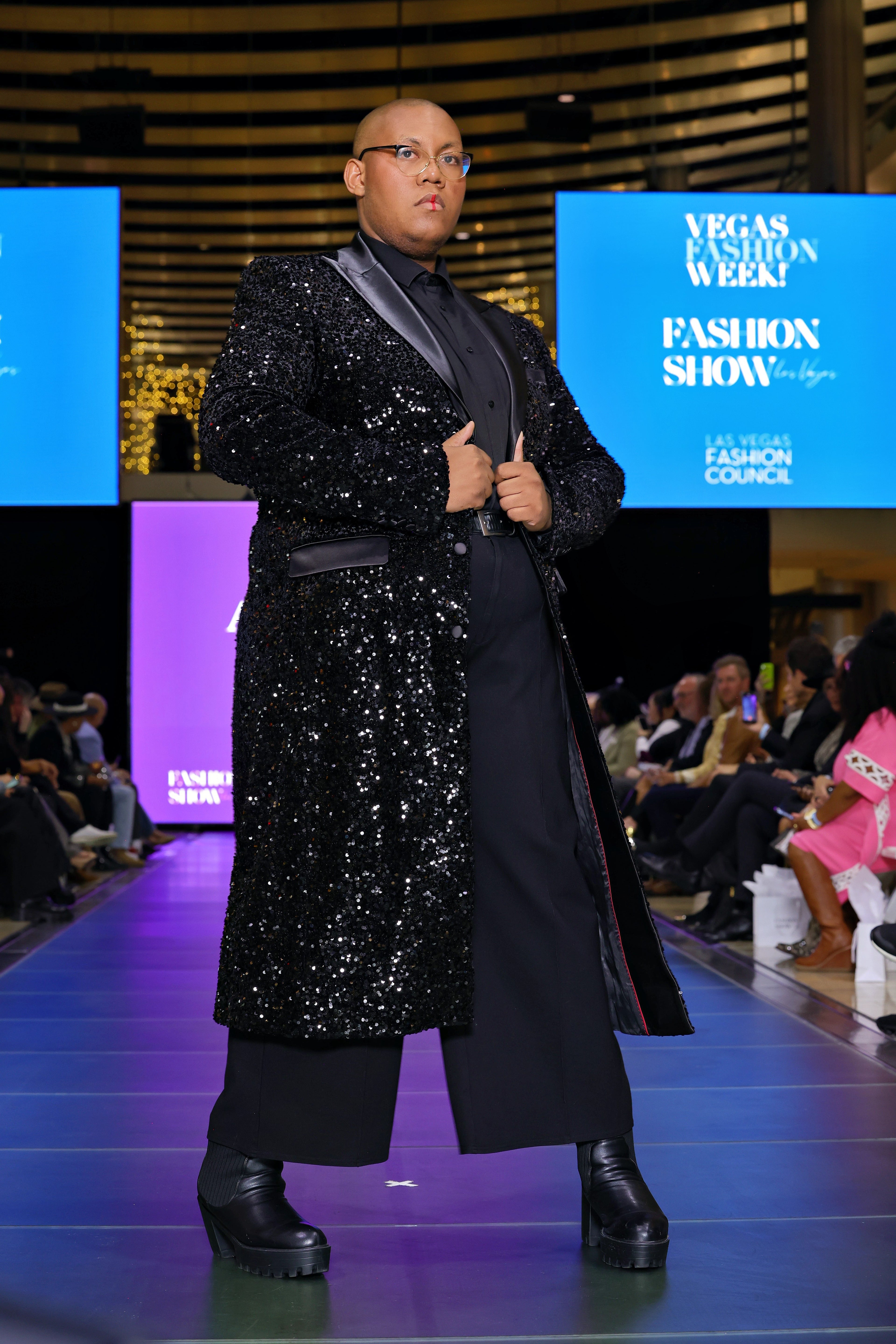 A model wearing a black sequin trench coat on a runway