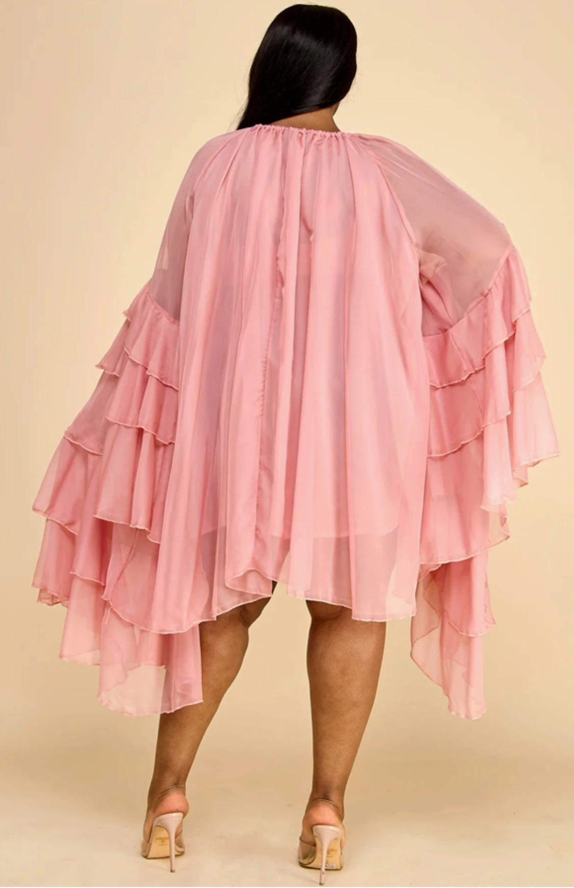 Woman wearing a pink ruffled sleeve dress against a beige background