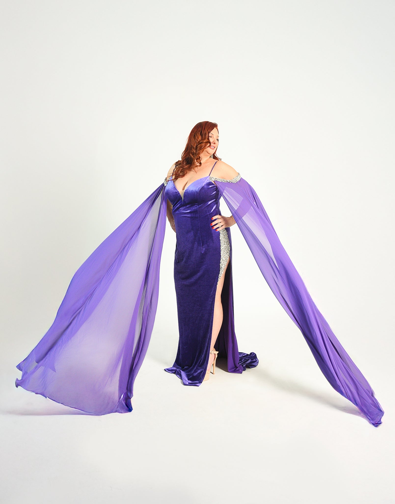 Formal gown with a high split adorned with crystal details. Cape sleeves. In a stretch velvet material. 