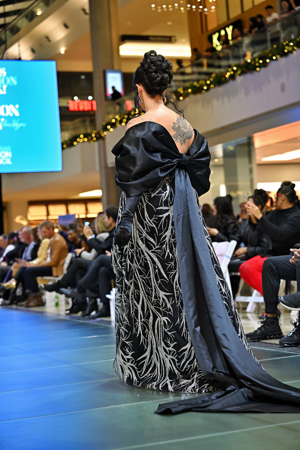 A woman wearing a black and silver  patterned gown with a bow shawl draped over her shoulder 