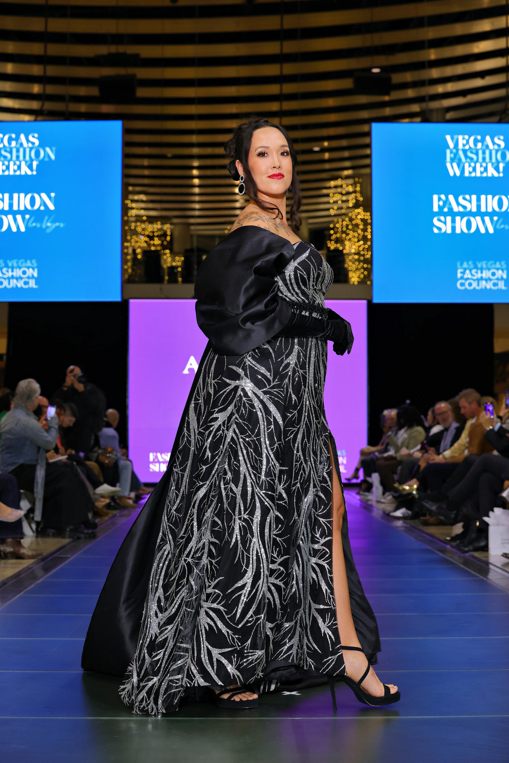 A woman in a black and silver patterned gown at a fashion show event.