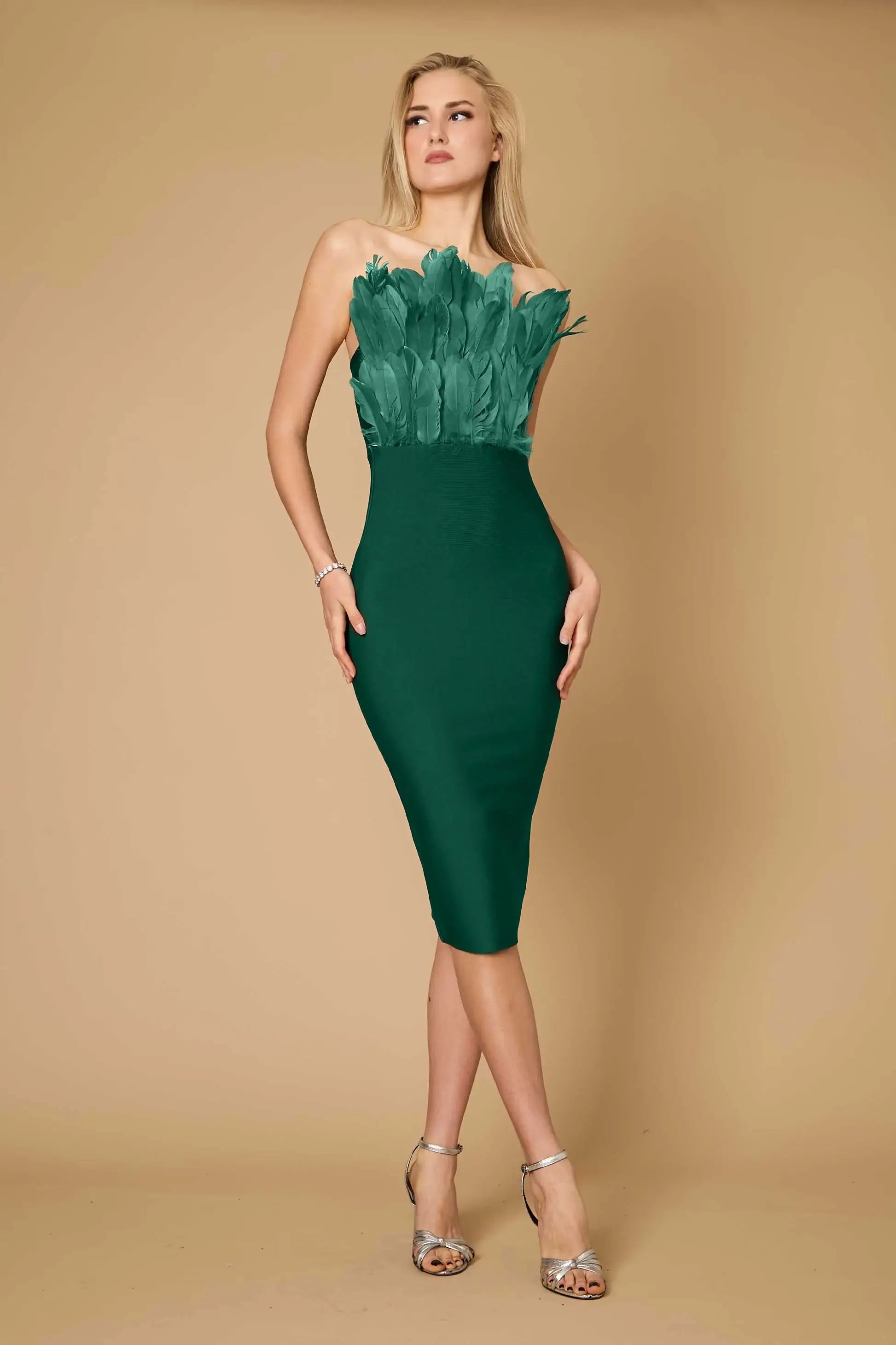 A woman wearing a green, sleeveless, fitted midi dress with feather detailing on the neckline.