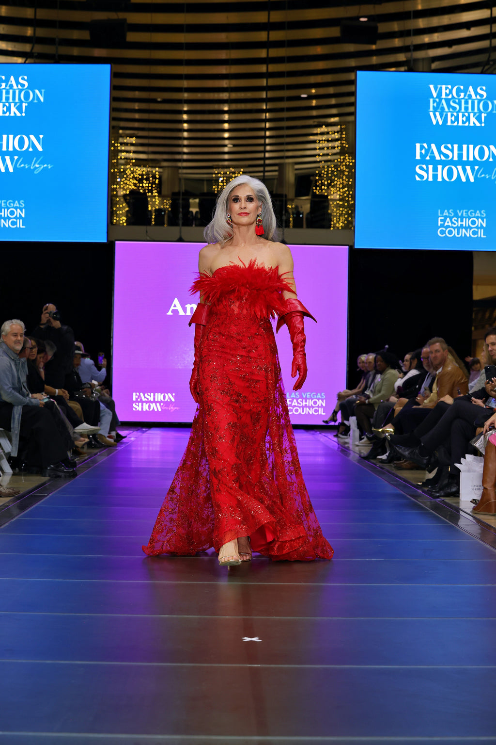 A woman in a red dress with feather details on a runway 